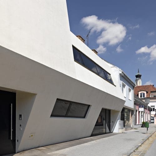lostinarchitecture_BUR_ White Monolith_Ordination und Wohnhaus von architekturaffinen Auftraggeber:innnen, geschlossene Straßenfassade, die sich im Gehsteigbereich für den Eintritt in die Arztpraxis öffnet.